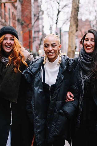Tre donne che si tengono a braccetto, sfondo della città